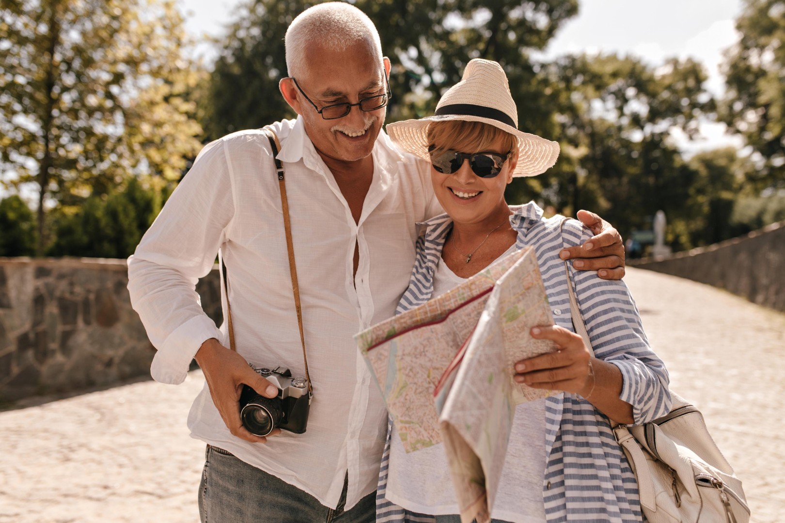 cheerful-man-with-grey-hair-light-shirt-jeans-with-camera-smiling-looking-map-with-blonde-lady-hat-blue-outfit-park (1).jpg